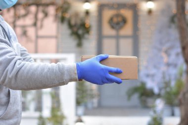 Coronavirus salgını sırasında tatiller için karantinaya alınan hediye ve paketlerin güvenli teslimatı. Bir kurye, tıbbi maske ve eldiven takmış bir gönüllü, bir kutu tutuyor. Mesaj için boşluk kopyala