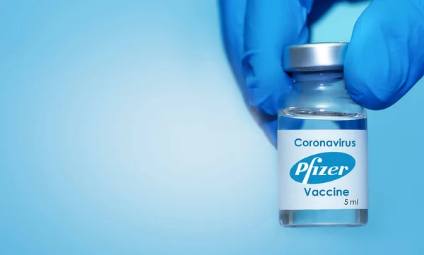 哈尔科夫 乌克兰 2020年11月23日 戴乳胶手套的医生或龙虾手拿着与辉瑞公司和Biontech公司合作开发的带有蓝色背景的考罗那韦疫苗 — 图库照片