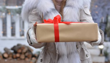 Coronavirus pandemiği sırasında karantinaya alınan hediye ve paketlerin güvenli teslimatı. Tıbbi maske takan gönüllü bir kız, pertakas ve üniforma içinde bir hediye kutusu var. Mesaj için yer kopyala