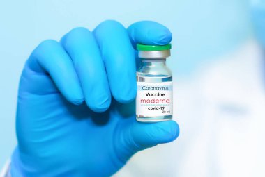 Harkiv. Ukrayna. 24 Aralık 2020. Moderna logosuyla Covid-19 aşısı. Eldivenli bir doktorun elinde mavi arka plan aşısı olan bir şişe var. Metin için alan kopyala.