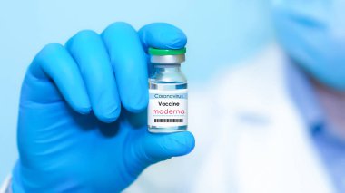Harkiv. Ukrayna. 24 Aralık 2020. Moderna logosuyla Covid-19 aşısı. Eldivenli bir doktorun elinde mavi arka plan aşısı olan bir şişe var. Metin için alan kopyala.