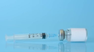 Mavi zemin üzerinde şırınga olan bir şişedeki aşı. Tıp, sağlık ve bilim konsepti. Coronavirus aşısı. Metin için alan kopyalama..