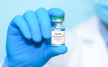 Harkiv. Ukrayna. 24 Aralık 2020. AstraZeneca logolu Covid-19 aşısı. Eldivenli bir doktorun elinde mavi arka planda koronavirüs aşısı olan bir şişe var...