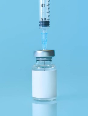 Mavi zemin üzerinde şırınga olan bir şişedeki aşı. Tıp, sağlık ve bilim konsepti. Coronavirus aşısı. Metin için alan kopyalama..