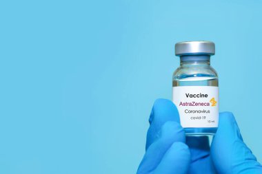 Harkiv. Ukrayna. 24 Aralık 2020. AstraZeneca logosuyla Covid-19 aşısı. Eldivenli bir doktorun elinde mavi arka planda koronavirüs aşısı olan bir şişe var. Metin için alan kopyala.