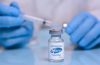 Harkiv. Ukrayna. 1 Şubat 2021. Tıbbi eldivenli bir doktorun arka planında Pfizer logoları olan Coronavirus aşı şişesi, bir şişe ve şırınga. Tıp, sağlık ve bilim kavramı.