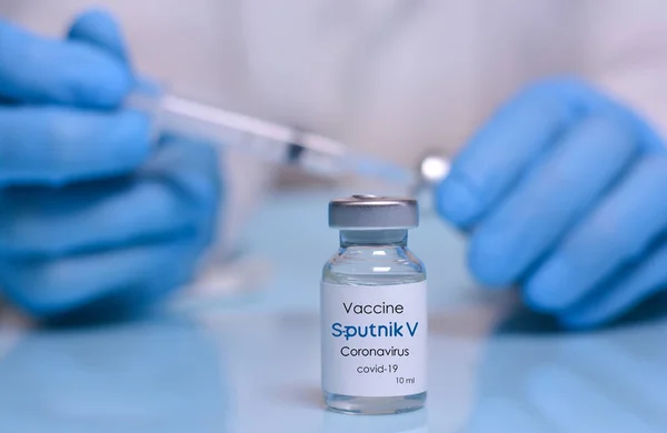 Harkiv. Ukrayna. 1 Şubat 2021. İçinde Sputnik V olan Coronavirus aşısı şişesi, tıbbi eldivenli bir doktorun arka planında logolar, bir şişe ve şırınga. Tıp, sağlık ve bilim kavramı.