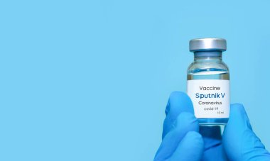 Harkiv. Ukrayna. 24 Aralık 2020. Sputnik v logo ile Covid-19 aşısı. Eldivenli bir doktorun elinde mavi arka plan aşısı olan bir şişe var. Mesaj için alan kopyala