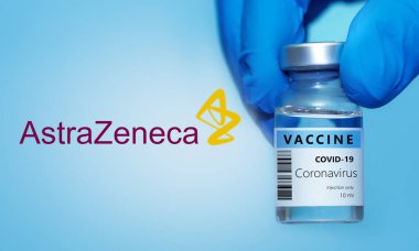 Harkiv. Ukrayna. 24 Aralık 2020. Covid-19 aşısı. AstraZeneca logosu. Tıbbi eldivendeki doktorun elinde mavi zemin üzerinde koronavirüs aşısı olan bir şişe var.