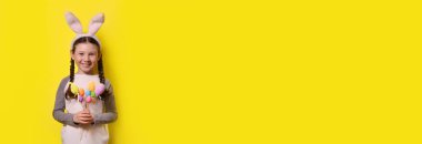 Paskalya tavşanı kulaklı komik mutlu kız sarı arka planda renkli Paskalya yumurtaları tutuyor. Mutlu Paskalyalar! Uzayı kopyala Pankart