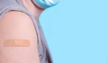 Tıbbi maskeli bir adam, mavi arka planda aşıdan sonra omuz yaması. İlaç konsepti, aşı, koronavirüs bağışıklığı, güvenli seyahat... Boşluğu kopyala