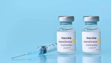 Harkiv. Ukrayna. 9 Ocak 2021. Şırınga, iki şişe koronavirüs aşısı mavi arka planda AstraZeneca logosu. Tıp, sağlık ve bilim konsepti. Metin için alan kopyala.
