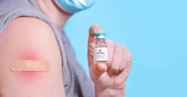 Harkiv. Ukrayna. 24 Aralık 2020. Tıbbi maskeli ve omzunda bir yama olan hasta Sinovac logosuyla birlikte bir şişe koronavirüs aşısı taşıyor. Sağlık hizmeti, aşı konsepti. Boşluğu kopyala