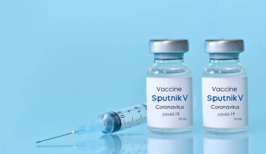 Harkiv. Ukrayna. 9 Ocak 2021. Şırınga, üzerinde mavi arka plan logosu olan iki şişe koronavirüs aşısı. Tıp konsepti, sağlık hizmeti. Metin için yer kopyalama..