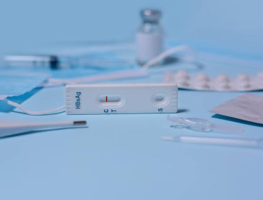Hepatit B Virüs Testi (HBsAg) için hızlı test kaseti, tıbbi maske, şırınga, termometre, mavi zeminde ilaç. Test negatif sonuç verdi. Boşluğu kopyala