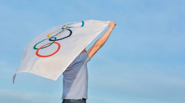 Kharkiv, Ukrayna. 23 Mayıs 2021 Olimpiyat bayrağını gökyüzüne karşı tutan bir erkek atlet. Tokyo Olimpiyat Oyunları 2020-2021