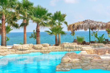 Güzel palmiye ağaçları ve deniz zemininde sazdan şemsiyeler olan tropik bir havuz. Tatil konsepti, seyahat. Güzel manzara