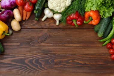 Ahşap arka planda bir sebze seti: havuç, patates, kabak, kırmızı biber, salatalık, sarımsak, domates, marul. Üst görünüm. Boşluğu kopyala