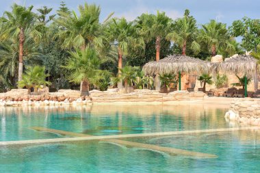 Güzel palmiye ağaçları ve deniz zemininde sazdan şemsiyeler olan tropik bir havuz. Tatil konsepti, seyahat. Güzel manzara