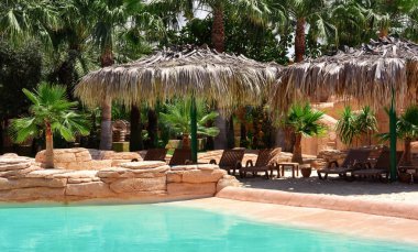 Havuzlu, güneşli, sazdan şemsiyeli, palmiye ağaçlı güzel tropikal manzara. Tropikal doğa, güzel manzara. Tatil ve tatil kavramı..