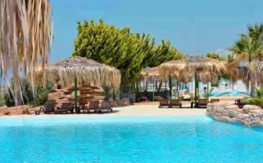 Güzel palmiye ağaçları ve deniz zemininde sazdan şemsiyeler olan tropik bir havuz. Tatil konsepti, seyahat. Güzel manzara