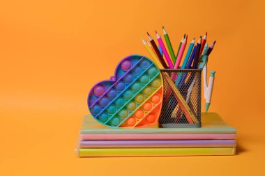 Okul malzemeleri: defterler, kitaplar, renkli kalemler, aç şunu - turuncu arka planda yeni popüler renkli silikon duyusal oyuncak antistresi. Okula dönelim. Boşluğu kopyala.