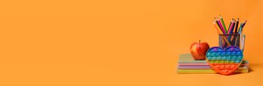 Okul malzemeleri: defterler, kitaplar, renkli kalemler, bir elma, patlat - turuncu arka planda yeni popüler renkli silikon duyusal oyuncak antistresi. Okula dönelim. Uzayı kopyala Pankart