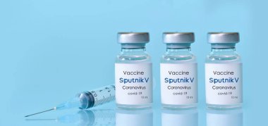 Harkiv. Ukrayna. 9 Ocak 2021. Şırınga, mavi zemin üzerinde Sputnik V logosu bulunan üç şişe Coronavirus aşısı. Tıp, sağlık konsepti. Text.t.Banner için alanı kopyala.