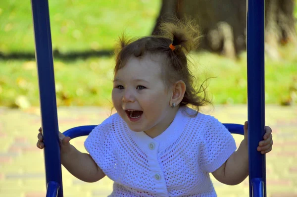 Fröhliches Mädchen reitet auf einer Schaukel auf dem Spielplatz — Stockfoto