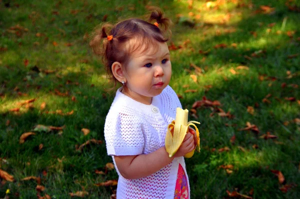 Liten flicka äter en banan i sommaren utomhus — Stockfoto