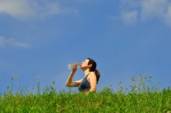 Flickan dricker vatten ur en flaska mot himlen — Stockfoto