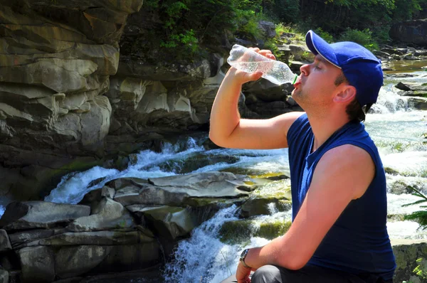 Man dricker ur en flaska vatten nära vattenfallet — Stockfoto