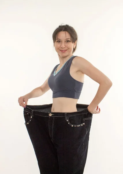 Женщина демонстрирует потерю веса на примере старых джинсов — стоковое фото