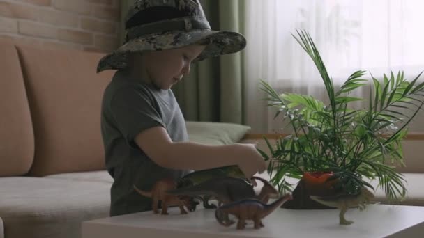 Niño Juega Con Figuras Dinosaurios Sobre Mesa Pequeño Explorador Sombrero — Vídeo de stock