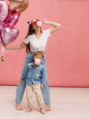 Genç insanlar dans ediyor, gülümsüyor ve pembe kalp şeklindeki balonların yanında eğleniyorlar. Pembe arka planda izole edilmiş.