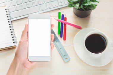 Cep telefonu beyaz bir ekran önünde tutan adam. Ve bir fincan kahve ve ofis malzemeleri arka plan
