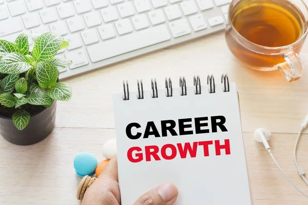 Man holding CAREER GROWTH message on book and keyboard with a hot cup of tea, macaroon on the table. Can be attributed to your ad. — Stock Photo, Image