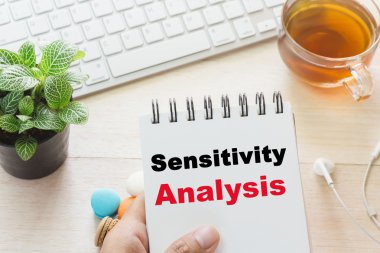 Man holding Sensitivity Analysis message on book and keyboard with a hot cup of tea, macaroon on the table. Can be attributed to your ad. clipart