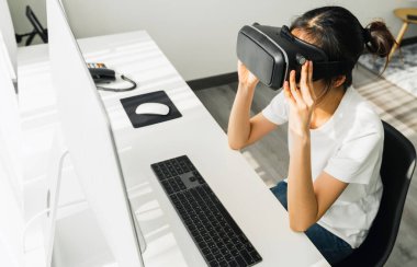 Sanal gerçeklik kulaklığı ve joystickler kullanan heyecanlı genç Asyalı kadın dijital teknolojinin bağlantılarını ve arayüzlerini kavrayabiliyor..