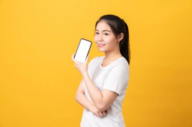 Neşeli, güzel Asyalı kadın elinde akıllı telefon tutuyor ve açık sarı arka planda mesaj yazıyor..