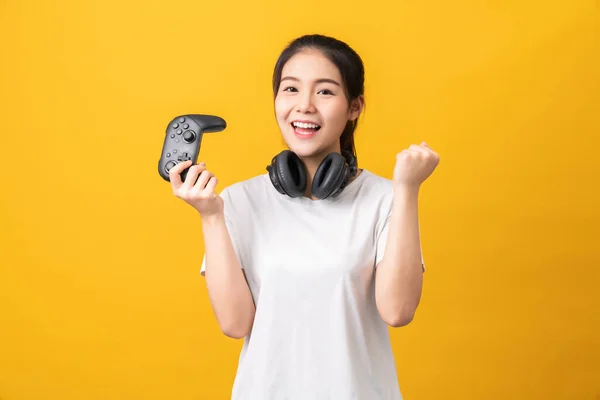 穿着休闲装的黄色T恤 头戴橙色背景耳机 玩电玩游戏的快乐美丽的亚洲女人 图库图片