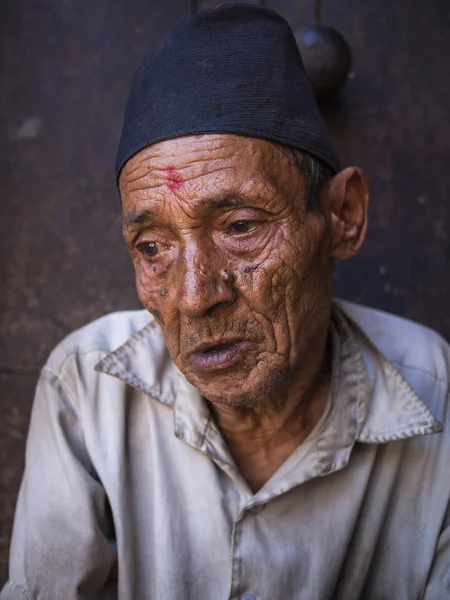 BHAKTAPUR, NEPAL-OCT 14, 2012: el anciano está sentado delante — Foto de Stock