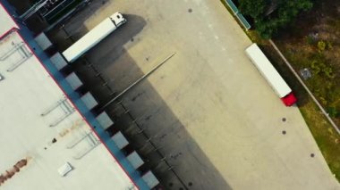 Lojistik parkındaki otoparkta yükleme merkeziyle birlikte bir depo boyunca giden yarı karavan kamyonlarının havadan çekimleri..