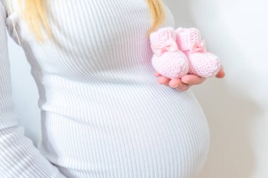 Hamile bir kadının karnındaki doğmamış bebek için küçük ayakkabılar.