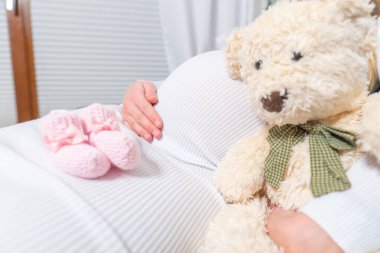 Hamile bir kadının karnındaki doğmamış bebek için küçük ayakkabılar.