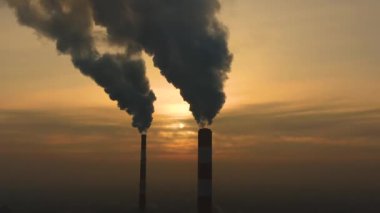 Hava kirliliği. Bitkinin bacalarından yükselen duman bulutları ve batan güneşin güzel sarı ışığı. İnsansız hava aracı çelik fabrikasının bacalarının üzerinde uçuyor..