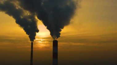 Hava kirliliği. Bitkinin bacalarından yükselen duman bulutları ve batan güneşin güzel sarı ışığı. İnsansız hava aracı çelik fabrikasının bacalarının üzerinde uçuyor..
