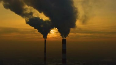 Hava kirliliği. Bitkinin bacalarından yükselen duman bulutları ve batan güneşin güzel sarı ışığı. İnsansız hava aracı çelik fabrikasının bacalarının üzerinde uçuyor..
