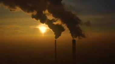 Hava kirliliği. Bitkinin bacalarından yükselen duman bulutları ve batan güneşin güzel sarı ışığı. İnsansız hava aracı çelik fabrikasının bacalarının üzerinde uçuyor..