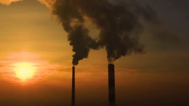 Hava kirliliği. Bitkinin bacalarından yükselen duman bulutları ve batan güneşin güzel sarı ışığı. İnsansız hava aracı çelik fabrikasının bacalarının üzerinde uçuyor..